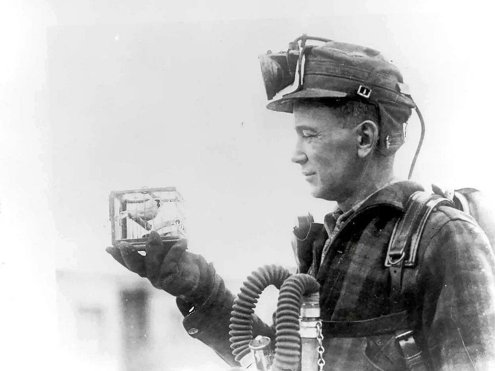 A miner holding a canary in a small cage in a coal mine
